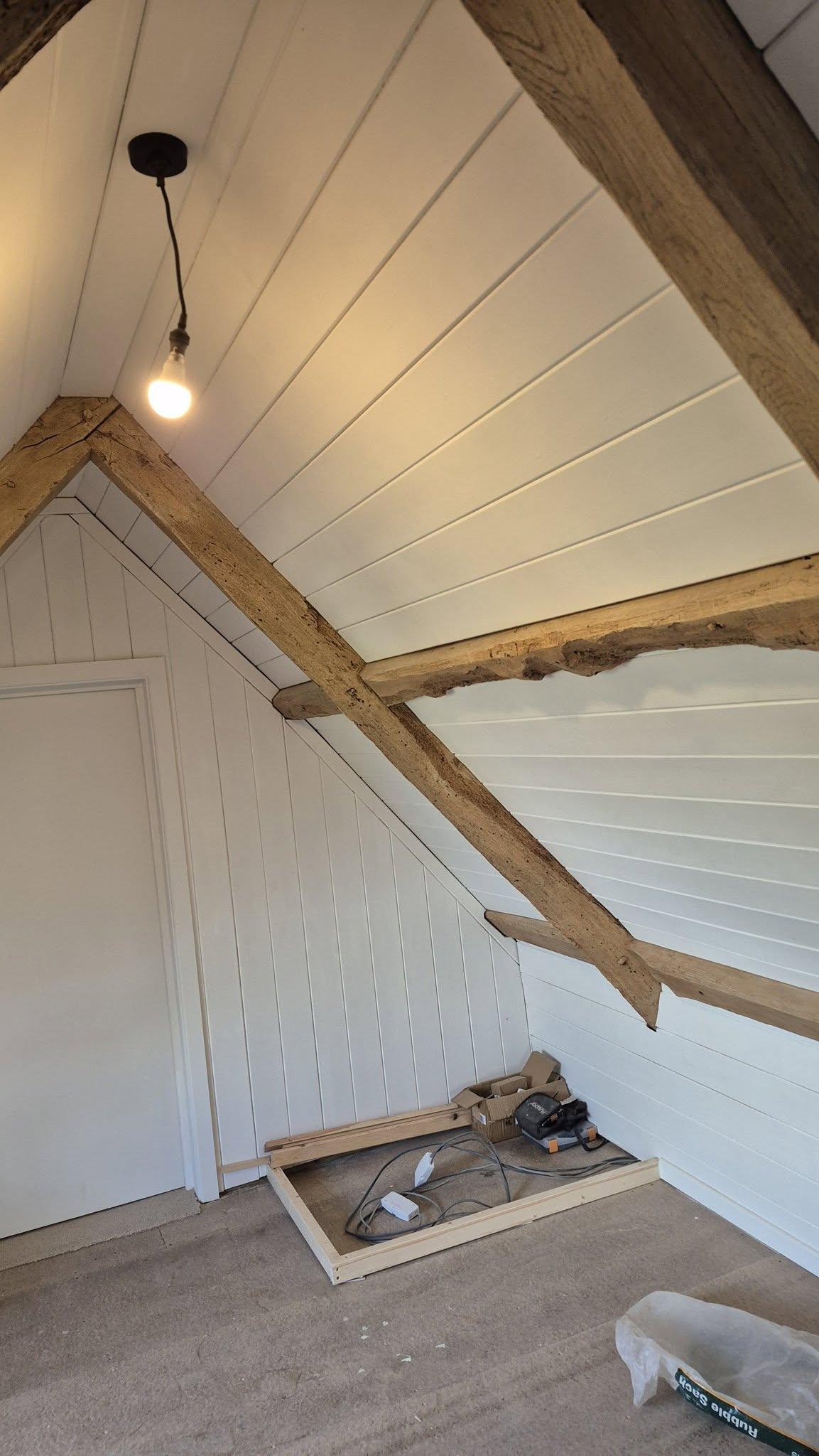 Loft space with white painted tongue-and-groove panelling and exposed oak roof beams