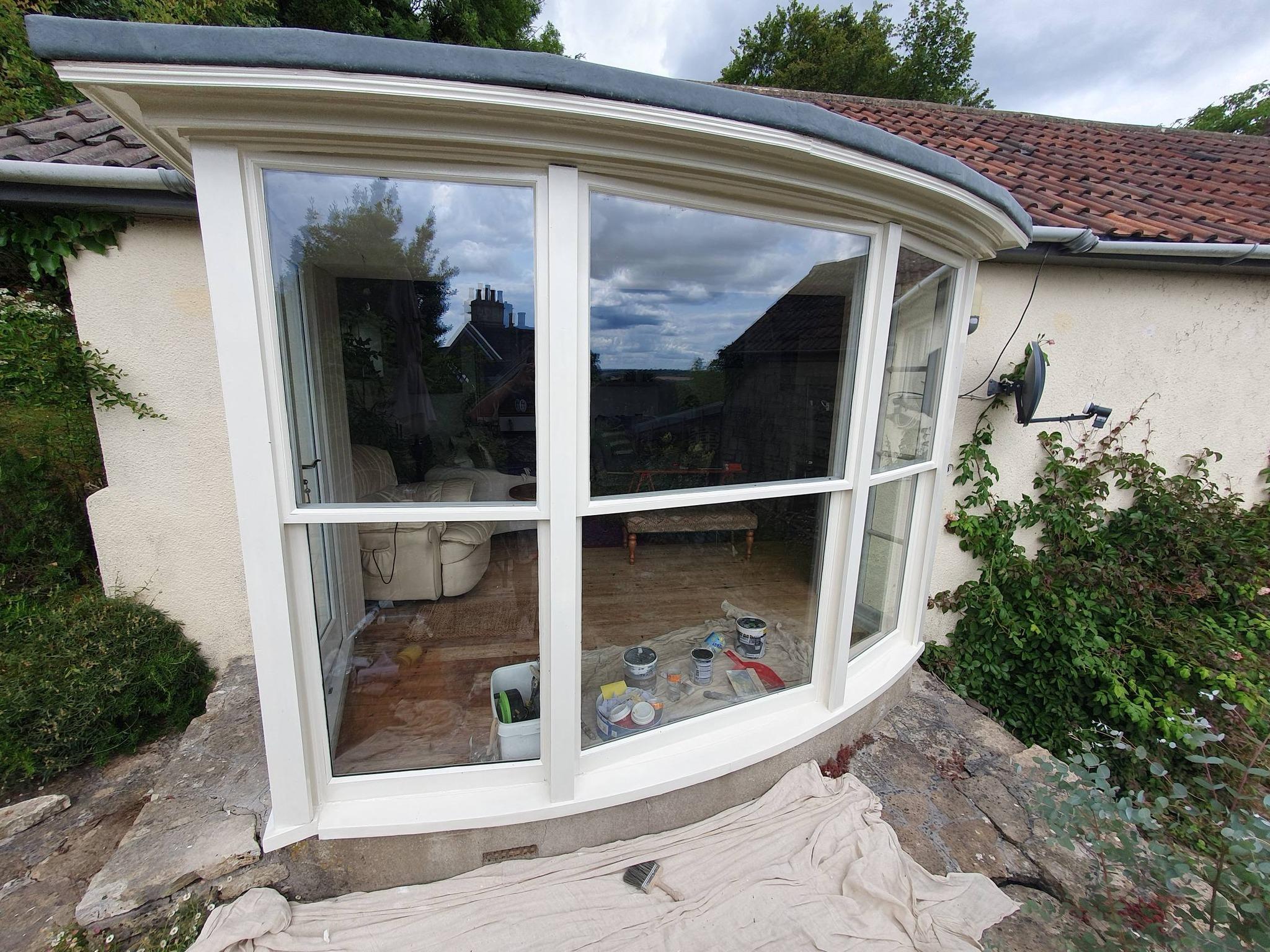 Curved bay window with freshly painted white timber frame on rendered cottage exterior