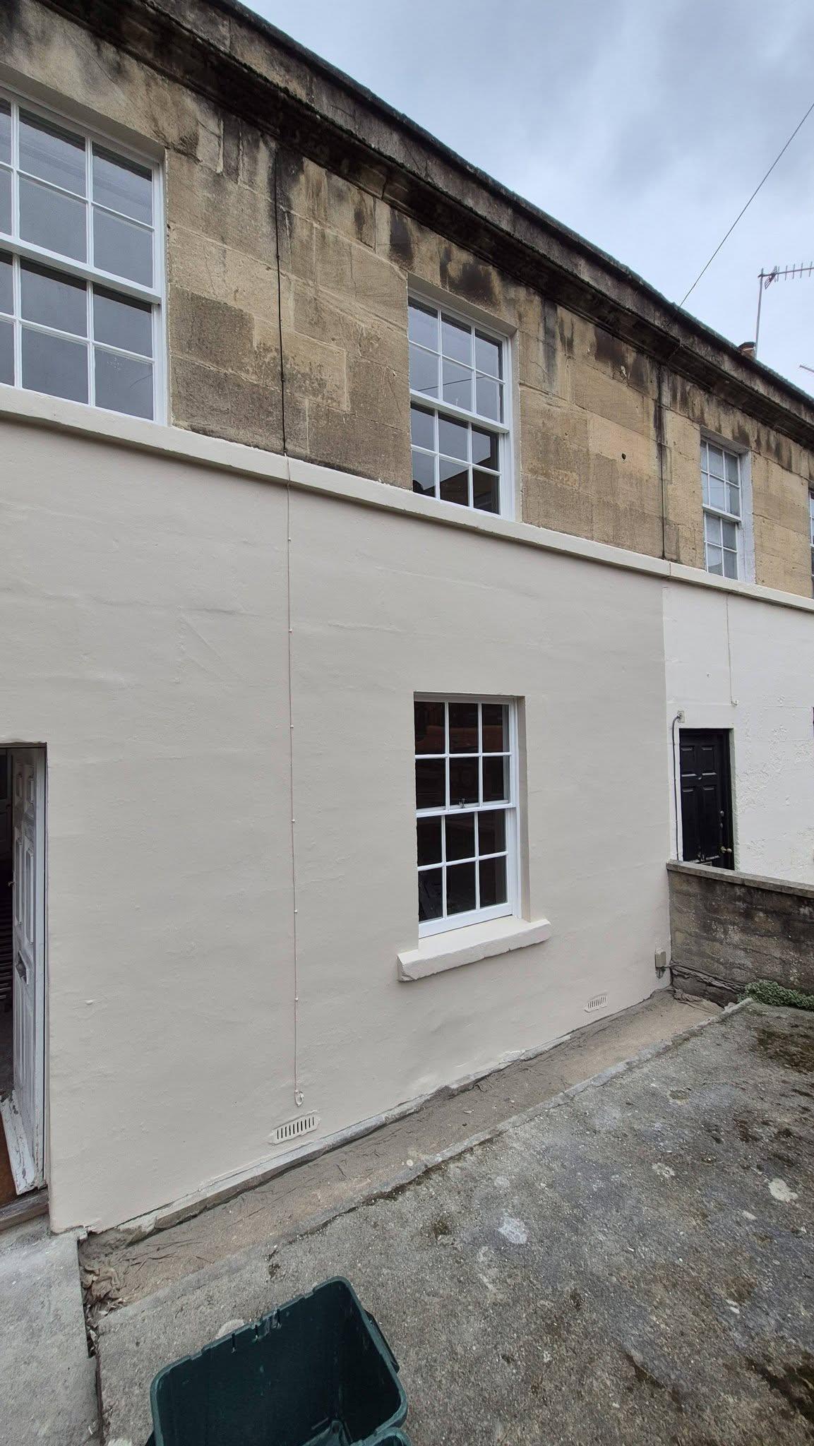 Exterior masonry wall freshly painted white below Bath stone with sash window