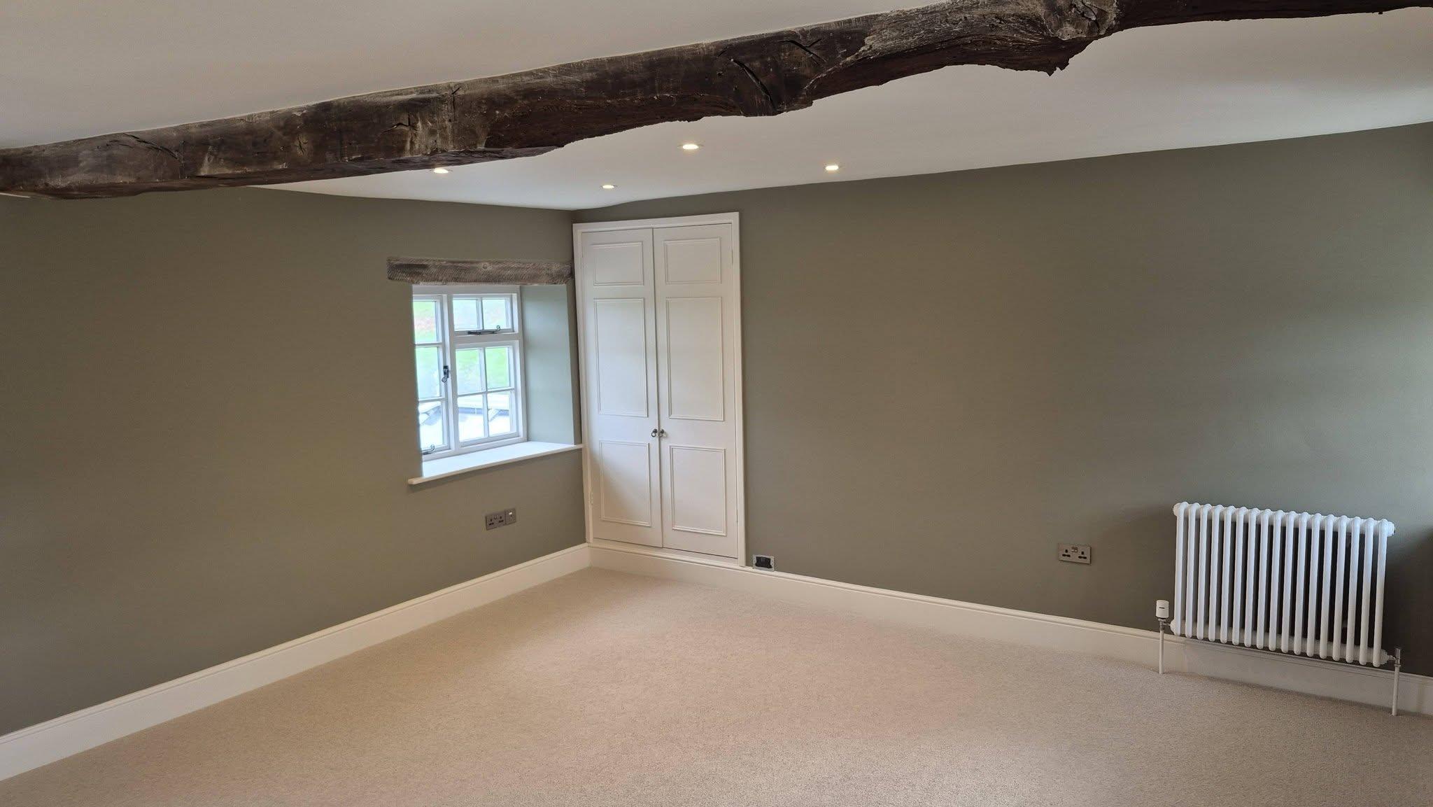 Sage green bedroom with white wardrobes, exposed oak beam and period window detail