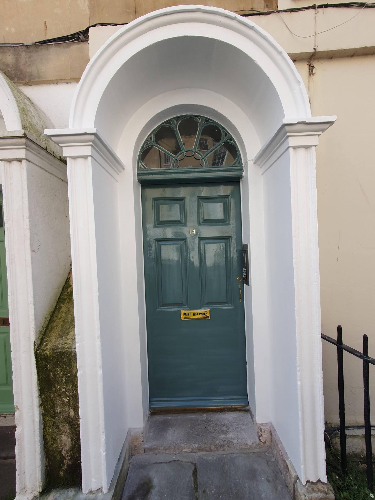 Freshly painted teal green Georgian front door with fanlight and white stone arch in Bath