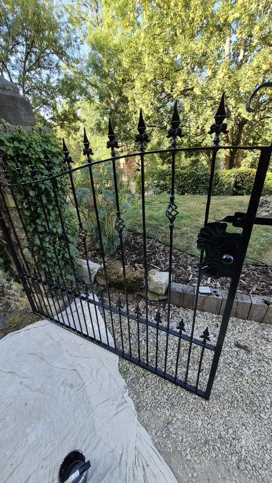 Repainted black wrought iron garden gate hung against a stone wall